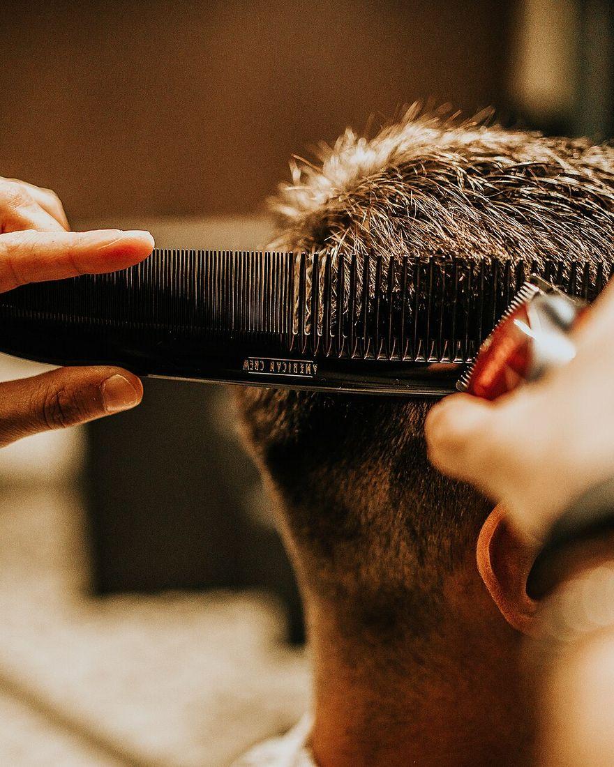 A barber cutting a client's hair with a comb and clippers